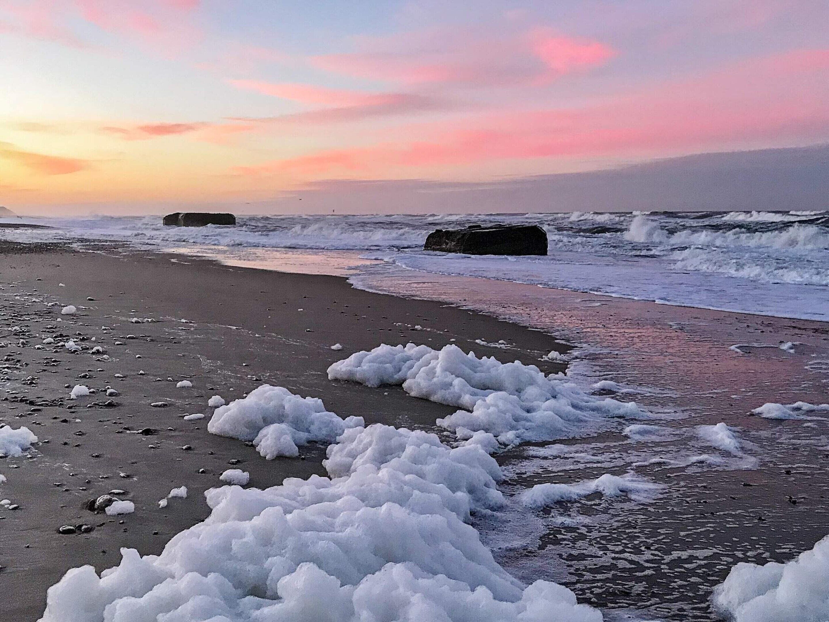 A beach with waves and rocks, under a sunset sky.