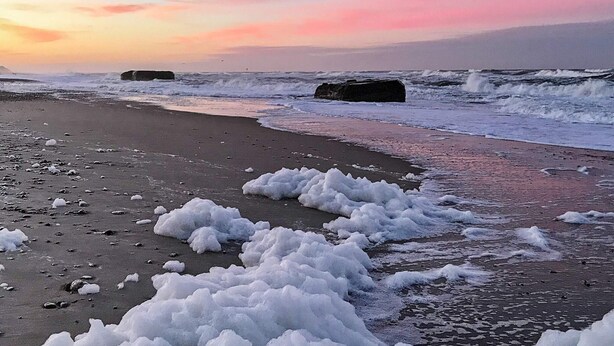 Una playa con olas y rocas, bajo un cielo al atardecer.