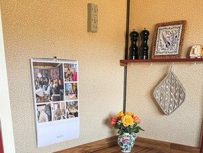 Una pared con un calendario, un florero con flores y una estantería con objetos decorativos.