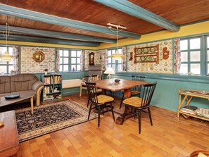 Una habitación acogedora con techo de madera, una mesa de comedor con sillas, un sofá, una estantería y una alfombra estampada.