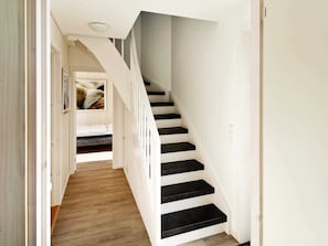 Eine Treppe mit weißen Wänden und schwarzen Stufen führt zu einem Schlafzimmer mit Bett und Fenster.