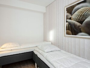 A small, single-bed room with a wooden wall and a framed picture of seashells. - Holiday Home in Wendtorf (Wendtorf)