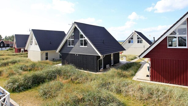 Een rij moderne, gelijkvloerse huizen met schuine daken, omringd door natuurlijke begroeiing.