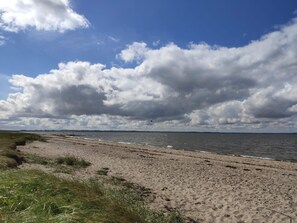Ein Strand mit breitem Sandstrand, einer Rasenfläche im Vordergrund und einem bewölkten Himmel.