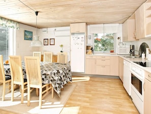 Une cuisine moderne avec des meubles en bois, une table à manger avec des chaises et une vue sur l’extérieur.