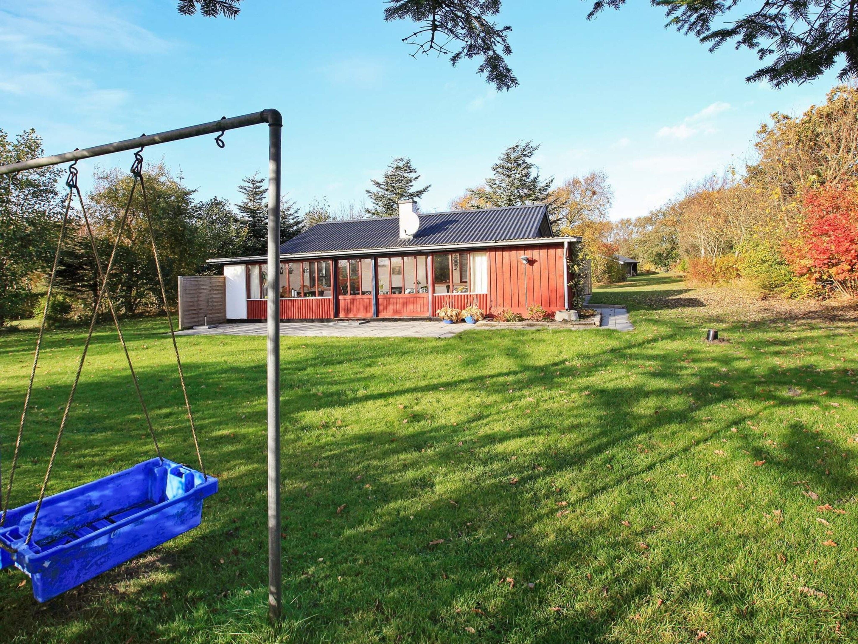 A red building with a porch, a swing set, and a blue swing seat in a grassy yard.