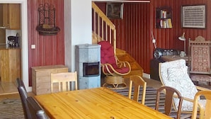 A dining area with a wooden table and chairs, a red armchair, a fireplace, and a staircase leading to another room.