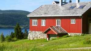 A red wooden house with a stone foundation, a sloped roof, and solar panels on the roof.