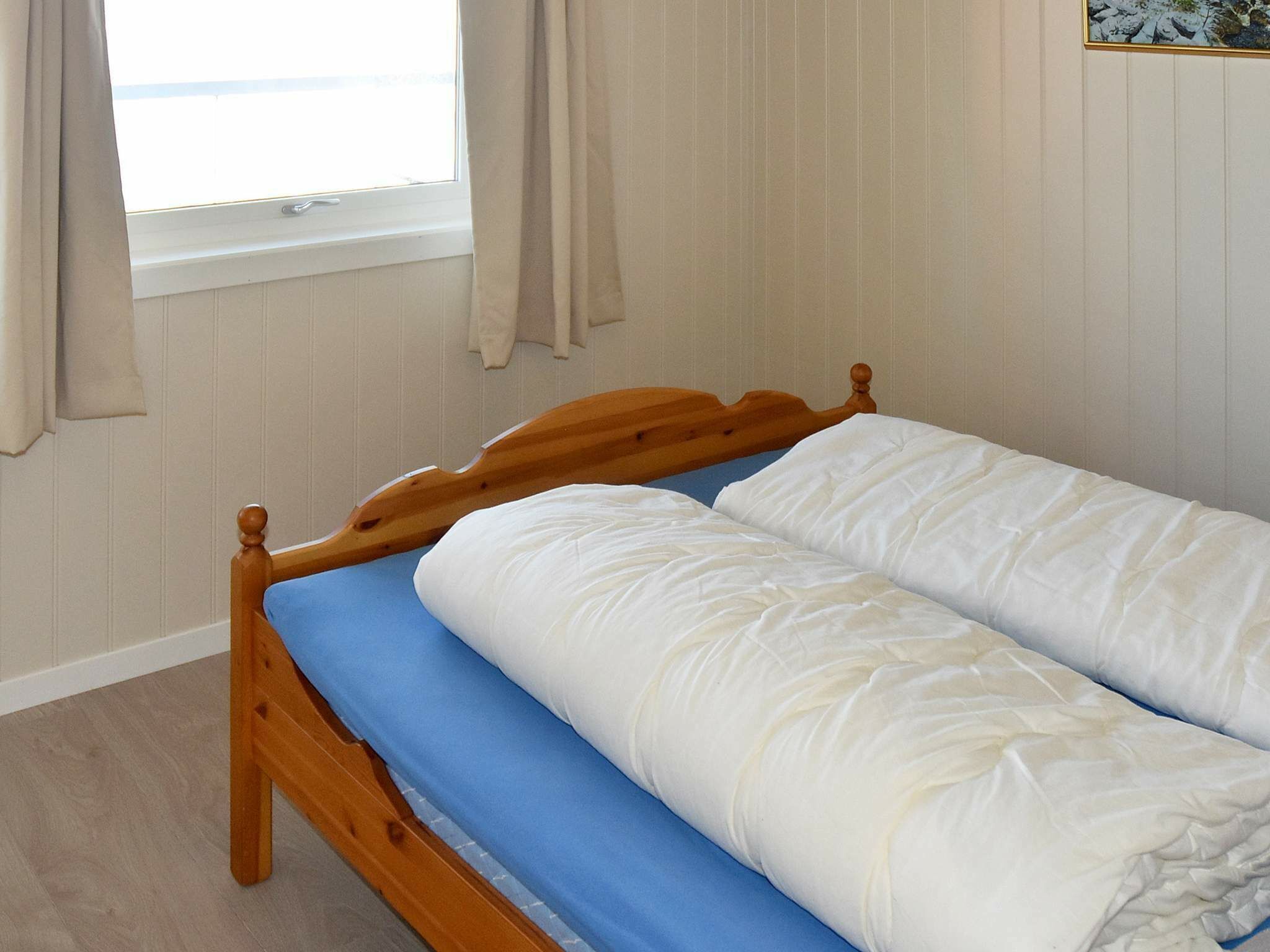 A single bed with a wooden headboard, a blue mattress cover, and white bedding.