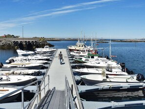 A marina with boats docked, a man walking on a pier, and a rocky shoreline in the background. - 11 Person Holiday Home in Farstad (Hustadvika)
