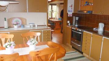 A kitchen with wooden cabinets, a dining table with chairs, a coffee maker, and a stove.