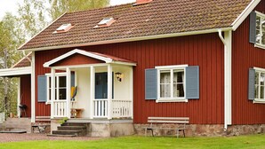 A red wooden house with a porch, two windows with shutters, and a chimney. - 6 Person Holiday Home in Paulistrom (Pauliström)