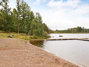 A lakeside area with a wooden dock extending into the water, surrounded by trees and a grassy bank. - 6 Person Holiday Home in Paulistrom (Pauliström)