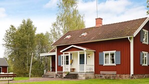 A red wooden house with a porch, white railings, and blue shutters. - 6 Person Holiday Home in Paulistrom (Pauliström)