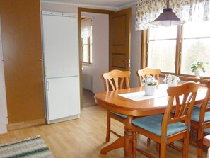 A dining area with a wooden table and chairs, a white refrigerator, and a window with curtains.