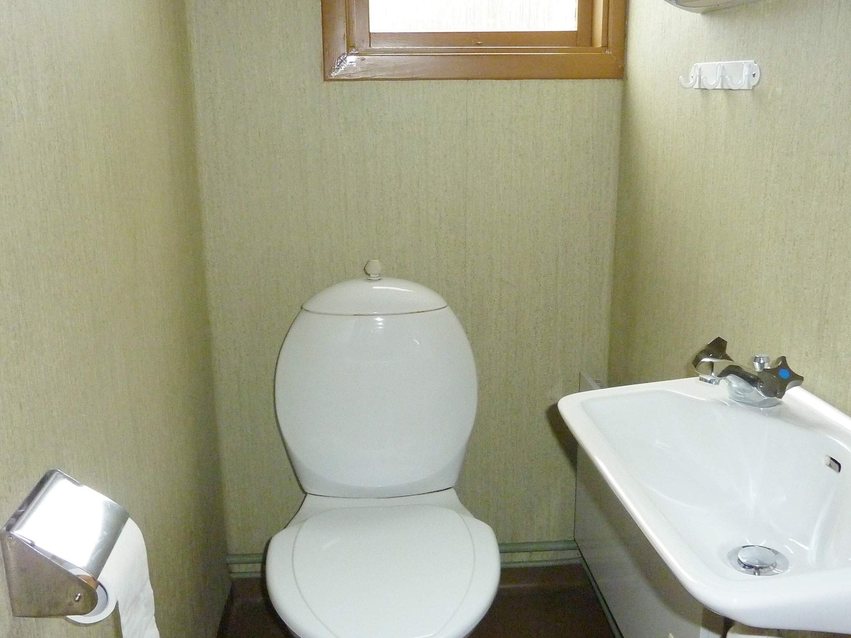 Un baño pequeño con inodoro, lavamanos y una ventana sobre el inodoro.