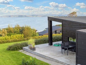 A modern outdoor deck with a view of the sea, a wooden pergola, and a seating area with a table and chairs.