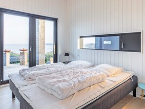 A bedroom with a bed, a nightstand, a lamp, and a view of the outdoors.