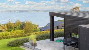A modern outdoor deck with a view of the sea, a dining area, and a wooden structure. - Simplistic Holiday Home in LÃ¸gstrup near Sea (Logstrup)