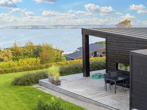 En modern uteplats med utsikt över havet, ett matområde och en träkonstruktion.