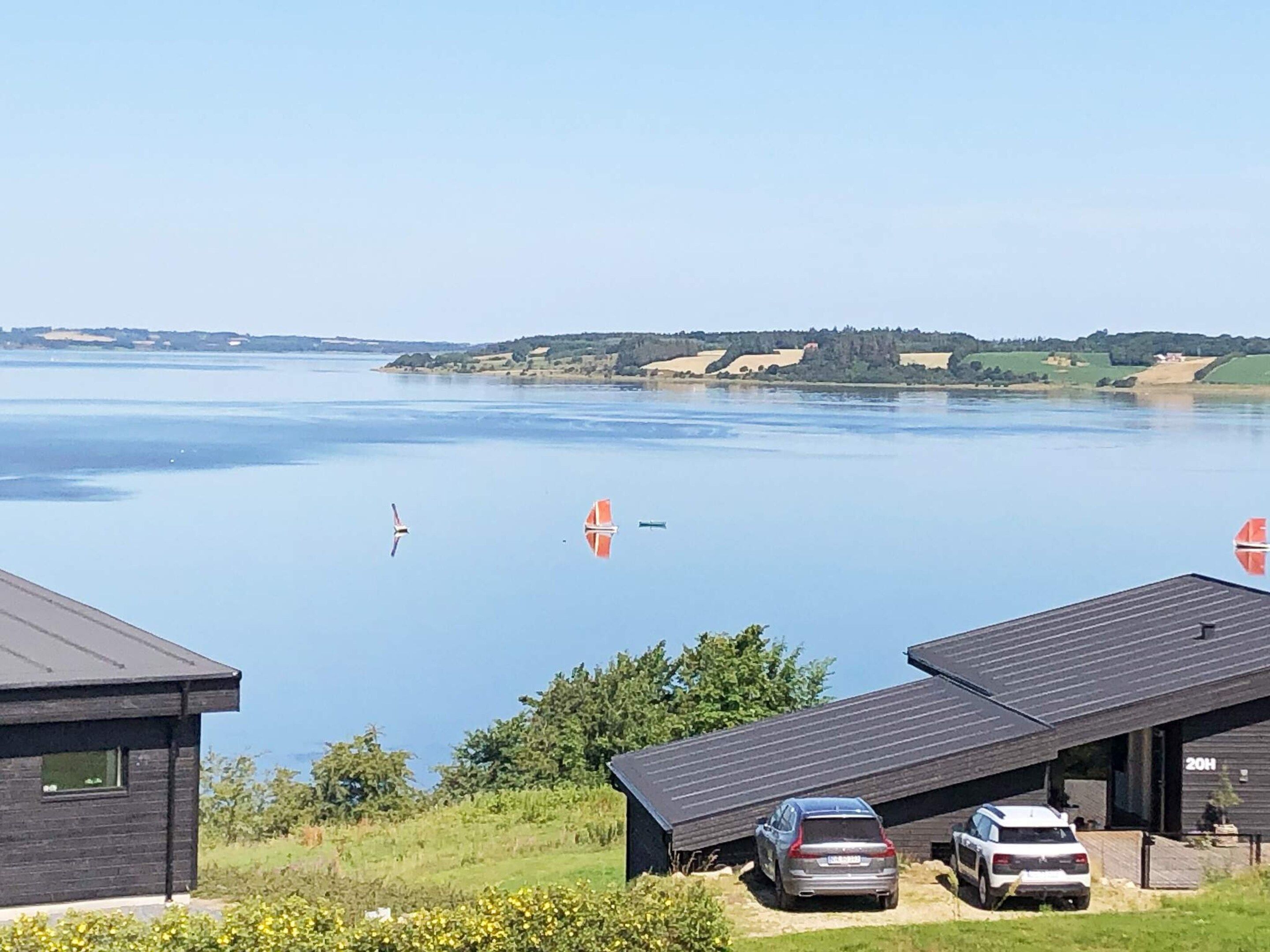 Una proprietà sul lago con vista sull'acqua, una barca a vela e un'auto parcheggiata in primo piano.