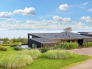 Ett modernt hus med ett platt tak, stora fönster och utsikt över havet.