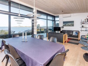 A modern dining area with a large table and chairs, a television, and a sofa.