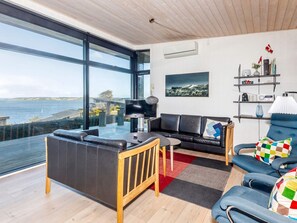 Una sala moderna con un ventanal grande, un sofá de cuero negro, un sillón azul y una mesa de centro de madera.