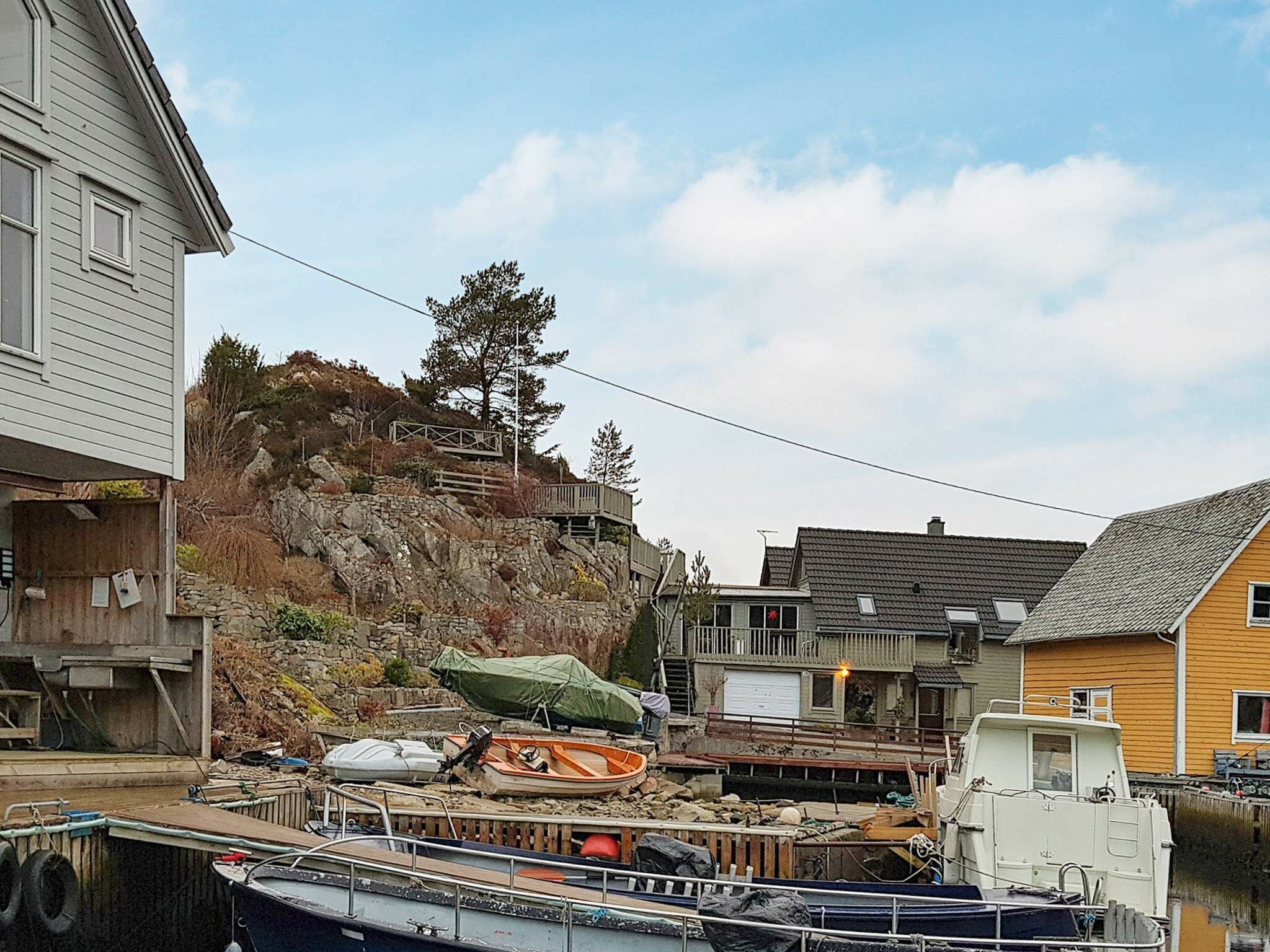 A waterfront property with boats docked, a rocky hillside, and residential buildings.