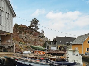 A waterfront property with boats docked, a rocky hillside, and residential buildings. - 10 Person Holiday Home in Urangsvåg (Bomlo)