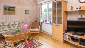 A cozy living room with a wicker sofa, a glass-top coffee table, a wooden cabinet with glass doors, a television, and a bookshelf. - 6 Person Holiday Home in Grenaa-by Traum (Grenaa)