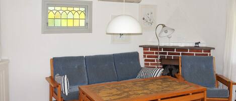 Un salon comprenant un canapé, deux fauteuils, une table basse, une cheminée et une fenêtre ornée de vitraux.