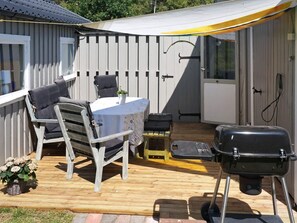 Une terrasse couverte avec une table et des chaises, un barbecue et une petite table agrémentée d’une plante.