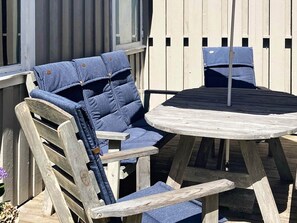 Une terrasse en bois avec une table ronde et deux chaises bleues dotées de coussins.