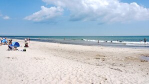 Una platja amb gent, alguns asseguts en cadiretes, i un veler a la distància.