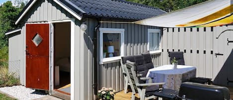 Eine kleine Holzhütte mit einer Holzterrasse, einem Grill und einem Tisch mit Stühlen.