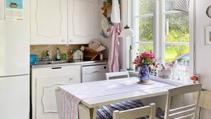 Une cuisine équipée d’une table à manger, de chaises, d’un réfrigérateur, d’un lave-vaisselle et d’une fenêtre donnant sur un espace verdoyant.