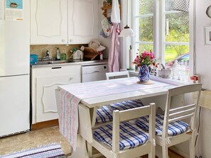 Una cocina con mesa, sillas, refrigerador, lavavajillas y ventana con vista a follaje.