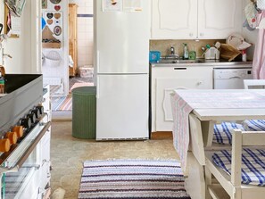 Cocina compacta con refrigerador, estufa, lavaplatos y un pequeño comedor con mesa y bancos.