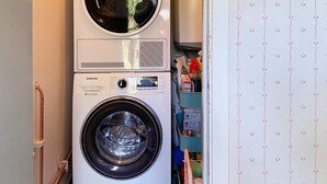 Un appareil combiné lave-linge et sèche-linge, de type « superposé », doté d’un panneau de commande numérique et d’une petite étagère située au-dessus.