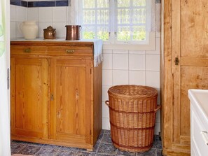 Una cocina con un armario de madera, una cesta de mimbre y una ventana con cortinas de encaje.