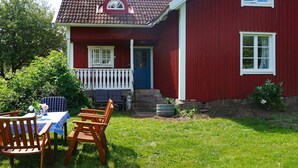 Une maison rouge avec un porche blanc, une porte bleue et un petit jardin agrémenté d’une table et de chaises.