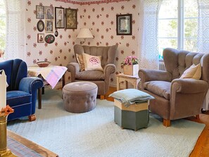 Una sala de estar acogedora con papel tapiz estampado, un sillón azul, un sillón marrón, un reposapiés a juego y una mesita auxiliar con una lámpara.