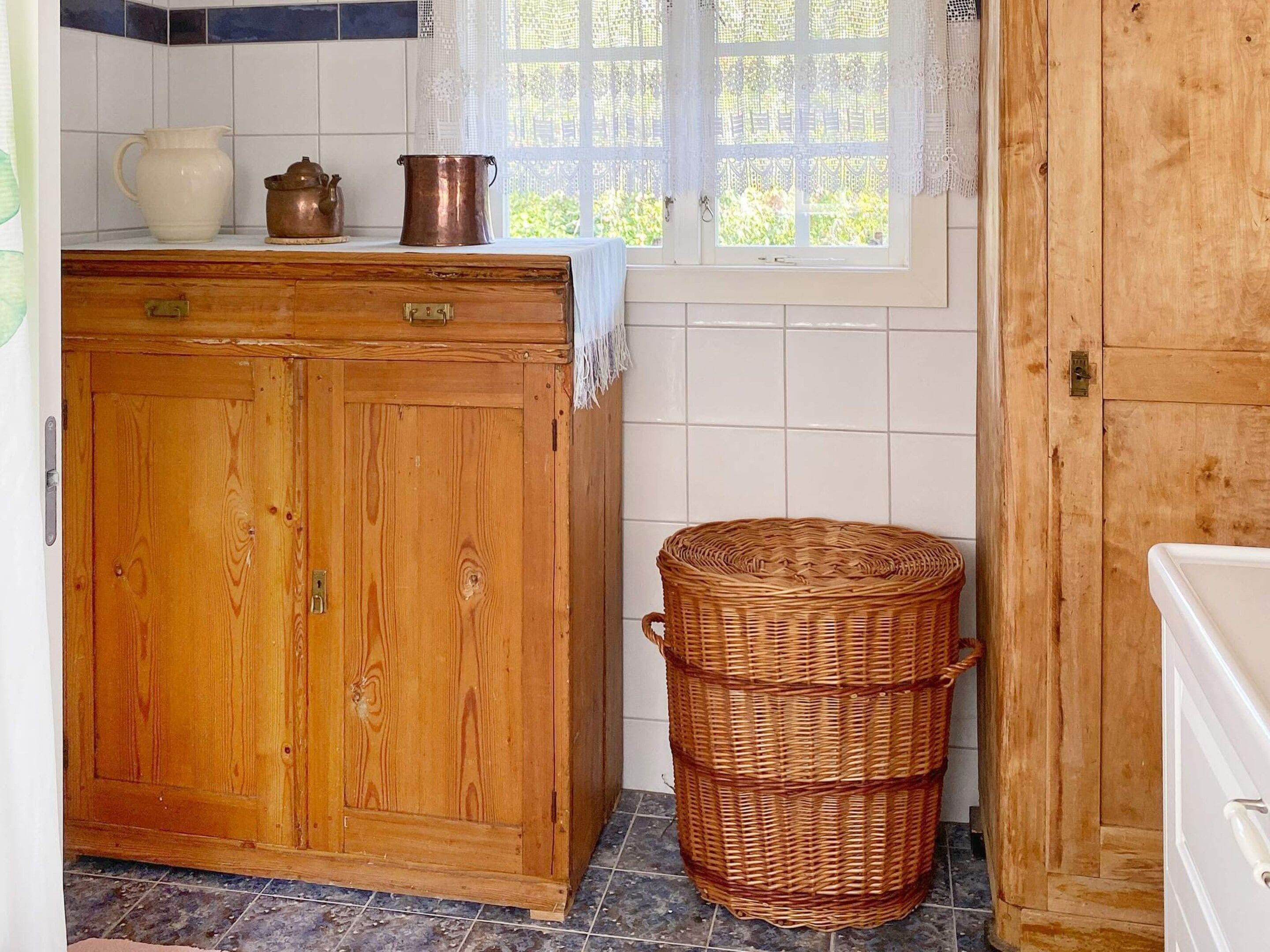 Una cucina con un armadietto in legno, un cesto di vimini e una finestra con tende di pizzo.