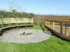 A circular stone patio with a central fire pit, surrounded by a wooden deck and a grassy area. - Sunlit Holiday Home in Funen near Sea (Otterup)