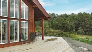 A wooden deck with outdoor seating and a covered area, surrounded by a forested landscape.