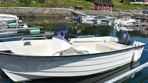 A small, white motorboat docked at a marina with a rocky shoreline and houses in the background. - Holiday Home in Vevang (Hustadvika)