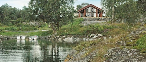 A house by a lake with boats, surrounded by trees and rocky terrain.