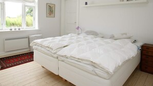 Un dormitorio con cama, ventana, radiador, estante con adornos y una puerta.