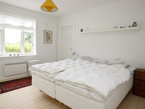 A bedroom with a bed, a window, a radiator, a shelf with decorative items, and a door.